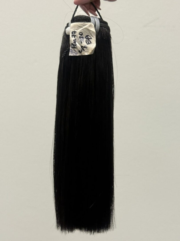 Long black straight hair bundle hanging against a white wall