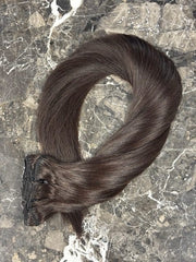 Dark brown straight clip-in hair extension laid in a loop on a marble surface
