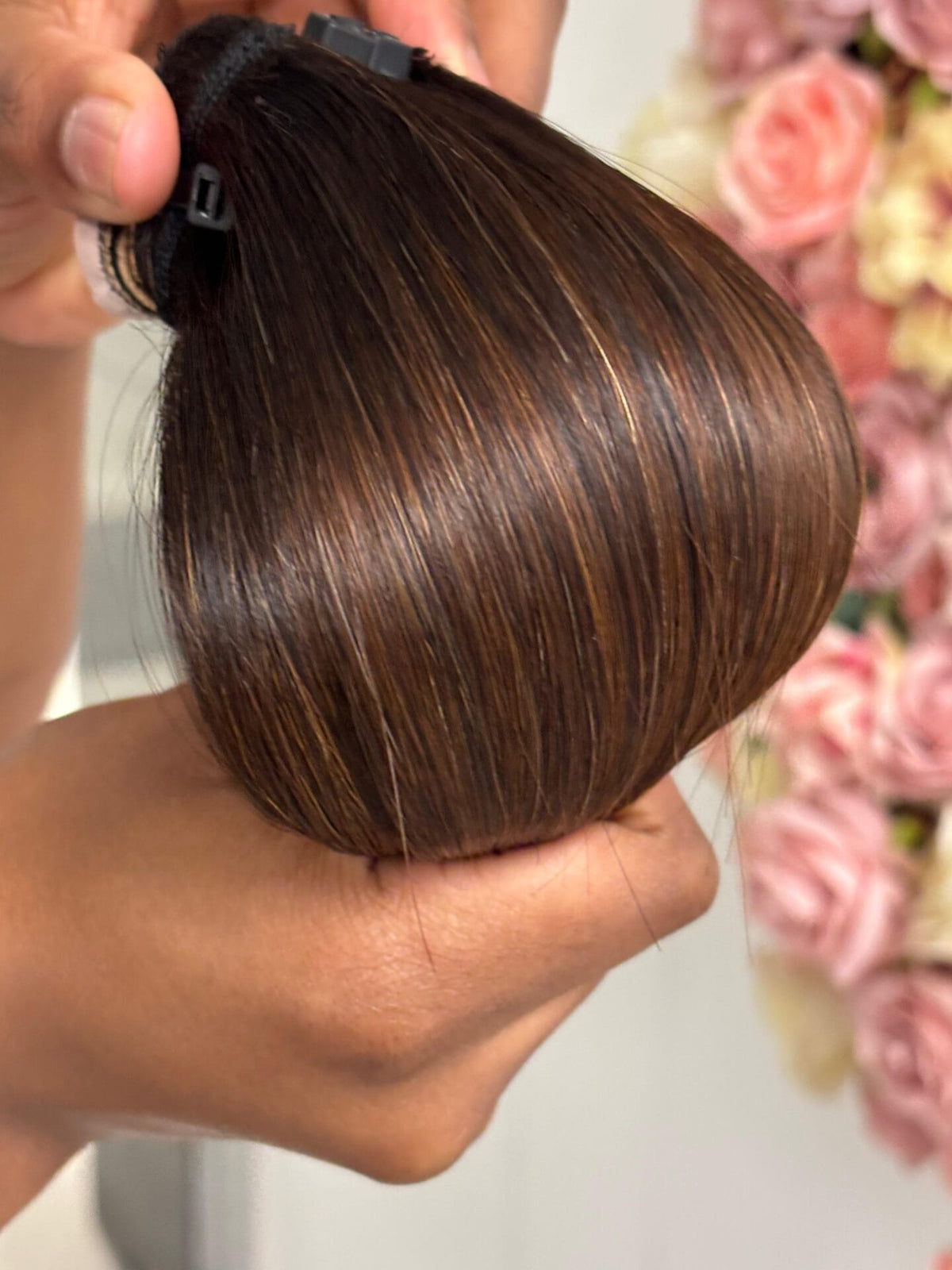 Warm brown straight hair bundle with darker roots folded over a hand