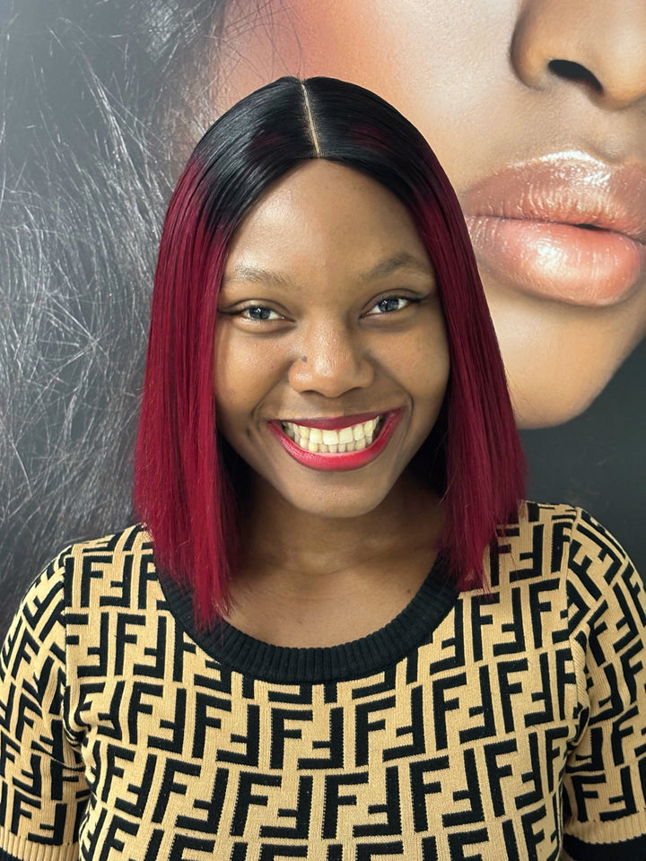 Front view of a model wearing a burgundy bob wig with black roots and a centre part